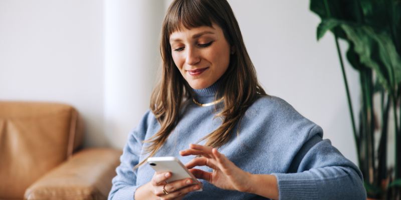 woman in gray sweater looking down at cellphone