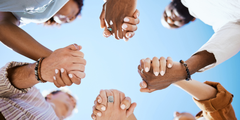 a few from below of people of different races holding hands in a circle